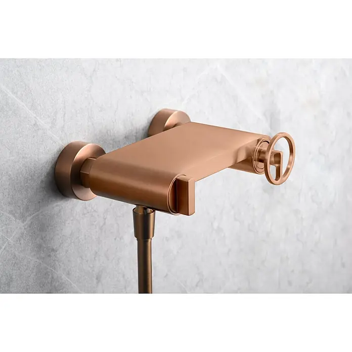 Imex Olimpo Grifo de ducha - Oro rosa - Primer plano de un accesorio de ducha de oro rosa con un diseño rectangular y un pomo redondo sobre una pared gris.