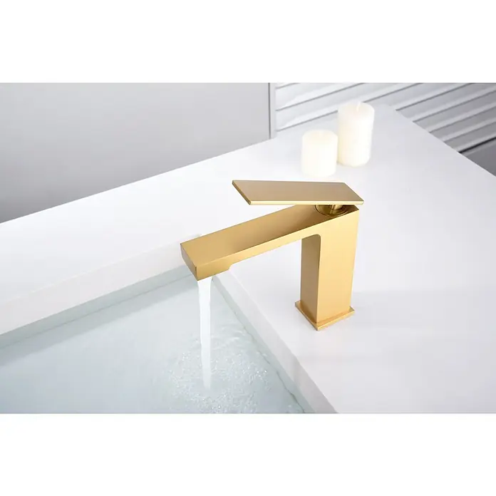 Imex Pisa Grifo de lavabo - Oro - Elegante grifo dorado con agua corriente sobre un lavabo blanco con velas al fondo.