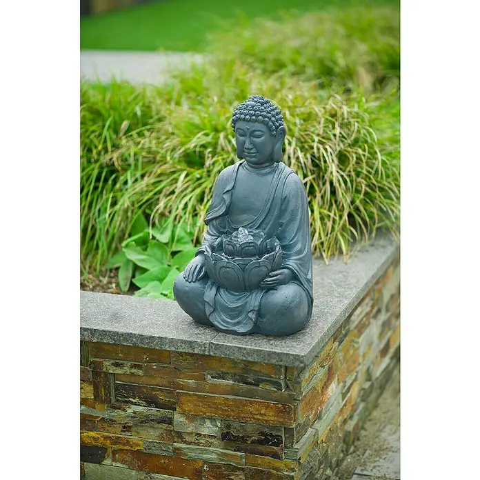 Ubbink AcquaArte Standbrunnen Sungai - 24 x 27,5 x 46 cm - Buddha-Brunnenstatue in sitzender Position auf einer Steinmauer, umgeben von Grün, eine friedliche Gartendekoration.