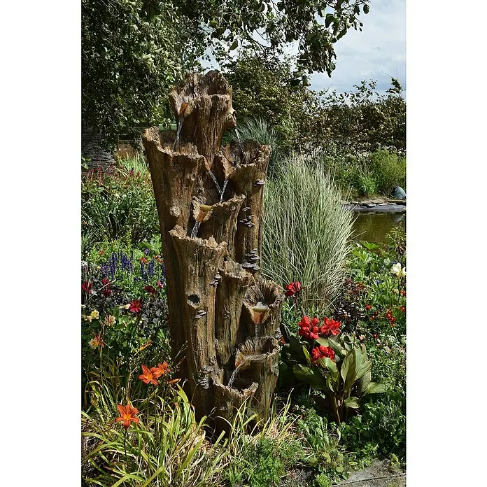 Ubbink AcquaArte Standbrunnen Tiros - 70 x 74 x 200 cm - Gartenszene mit einem dekorativen, künstlichen Baumstamm-Brunnen, der Wasser über mehrere Ebenen leitet, umgeben von üppigen Blumen und Pflanzen.