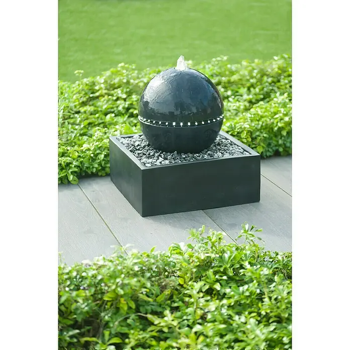 Gartenbrunnen Tripoli - 50 x 50 x 53 cm - Ein faszinierender Kugelbrunnen mit LED-Beleuchtung in einem schlichten, schwarzen Becken, umgeben von üppigem Grün, ein Blickfang für jeden Garten.