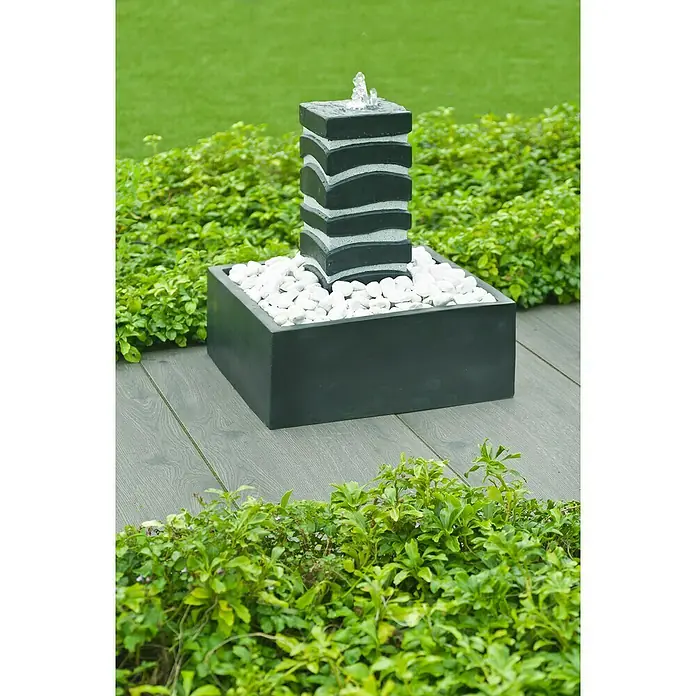 Ubbink AcquaArte Standbrunnen Borgo - 50 x 50 x 40 cm - Moderner Gartenbrunnen mit einem schwarzen, wellenförmigen Turm und weißen Kieselsteinen in einem quadratischen Becken, umgeben von üppigem Grün.