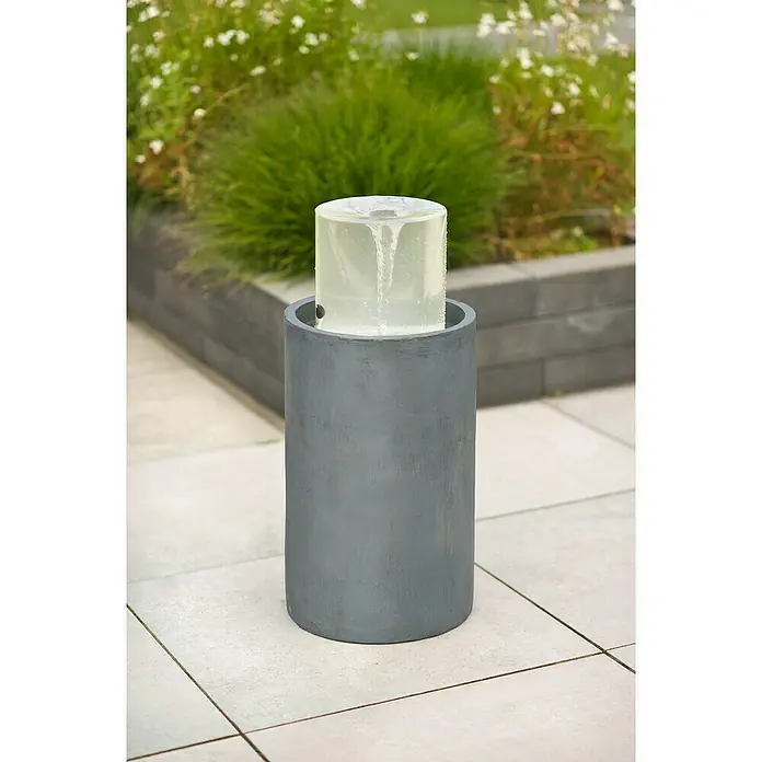 Ubbink AcquaArte Standbrunnen Salemi - 30 x 30 x 67 cm - Nahaufnahme eines zylindrischen Vortex-Brunnens im Freien, mit Wasserwirbel im durchsichtigen Zylinder, der auf einem grauen Sockel steht.