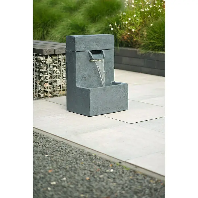 Ubbink AcquaArte Standbrunnen Posada - 40 x 30 x 61 cm - Nahaufnahme eines grauen Wasserspiels im Freien auf Steinfliesen, umgeben von üppigem Grün.