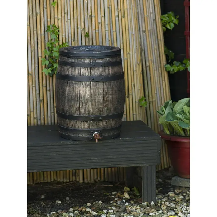Nature Regentonne - 50 l, Braun - Regentonne in Holzfassoptik auf einer dunklen Holzbank im Garten, umgeben von Pflanzen und Kies. Praktisch und dekorativ!