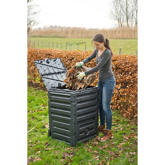 Nature Komposter - 300 l, 60 x 60 x 90 cm - Frau entleert Laub in einen schwarzen Kompostbehälter im Garten. Der Behälter ist aus robustem Kunststoff gefertigt.