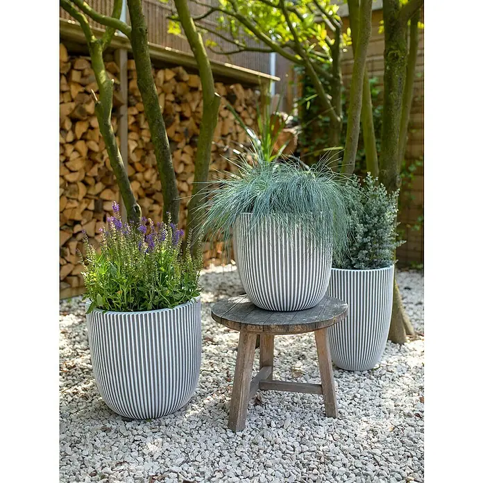 Capi Europe Nature Rib NL Pflanzgefäß Groove - Außenmaß (Ø x H): 35 x 35 cm, Elfenbein, Kunststoff - Stilvolle Außendekoration mit drei gestreiften Pflanzgefäßen, die mit verschiedenen Pflanzen bepflanzt sind, auf einem Kiesweg.
