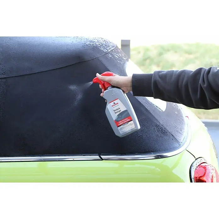 Nigrin Performance Verdeckreiniger - 500 ml, Textile Cabrioverdecke - Auf dem Bild wird ein NIGRIN Verdeck-Reiniger auf ein schwarzes Stoffverdeck eines hellgrünen Autos gesprüht, um es zu reinigen und zu pflegen.
