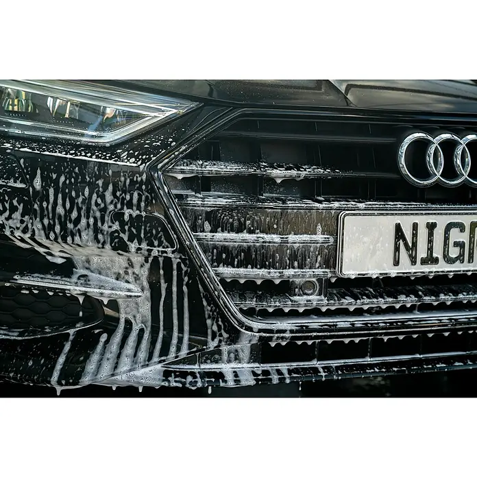 Nigrin Auto-Shampoo Power - 1 l, Minze, Grapefruit - Nahaufnahme eines schwarzen Audi-Grills mit dem Audi-Logo, der mit Schaum bedeckt ist. Das Auto wird gerade gewaschen.