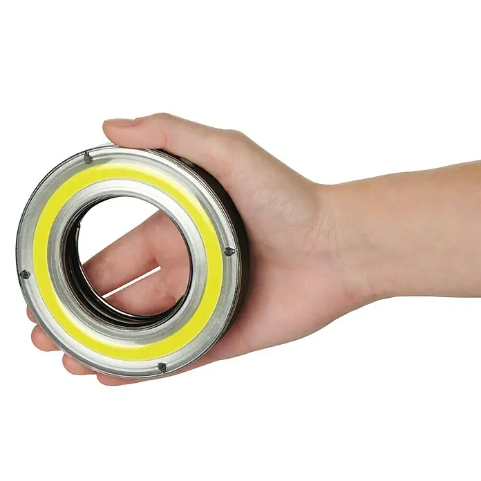 Hama Mobiles LED-Licht Ultra Camping - Batteriebetrieben, Schwarz, Höhe: 2 cm - Eine Hand hält eine ringförmige LED-Lampe. Das Licht ist gelb und das Gehäuse ist aus Metall.