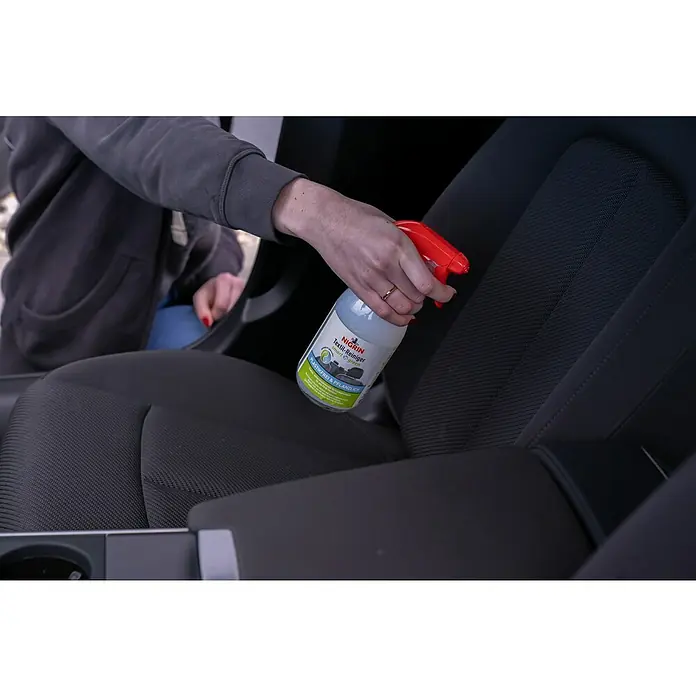Nigrin Textilreiniger SMART `N GREEN - 500 ml - Eine Person sprüht Nigrin Textil-Reiniger Smart & Green auf einen Autositz. Das Produkt ist plastikfrei und pflanzlich.