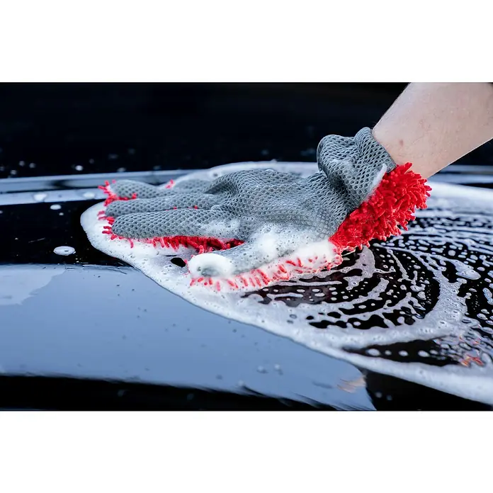 Nigrin Performance Auto-Shampoo Ceramic - 500 ml - Eine Hand mit einem Waschhandschuh reinigt ein schwarzes Auto mit Schaum, wobei der Handschuh die Oberfläche sauber wischt.