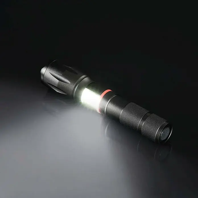 Hama Taschenlampe Solid Pro - 200 lm - Nahaufnahme einer schwarzen taktischen Taschenlampe mit eingeschaltetem Seitenlicht auf einer reflektierenden Oberfläche.