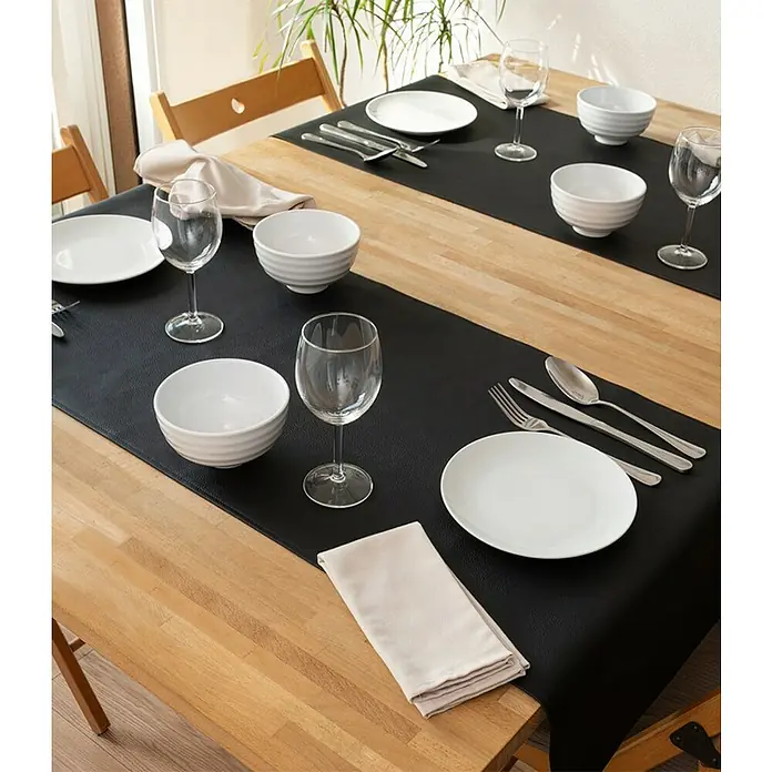 Tischläufer Monaco - 140 x 45 cm, Black - Detailaufnahme eines gedeckten Tisches mit Tellern, Gläsern, Schüsseln und Servietten auf einer stilvollen, schwarzen Tischdecke.