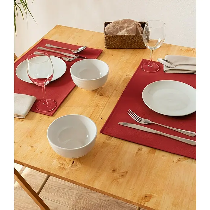 Tisch-Set Monaco - Red, 45 x 30 cm - Ein gedeckter Holztisch mit roten Platzsets, weißem Geschirr, Gläsern und Besteck. Eine Brotkorb aus Korbgeflecht rundet das Arrangement ab.