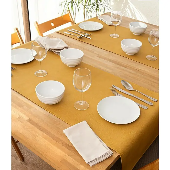 Tischläufer Monaco Raw - Ocre, 140 x 45 cm - Eine Nahaufnahme eines gedeckten Tisches mit Tellern, Schüsseln, Gläsern und Servietten auf einem senffarbenen Tischläufer.