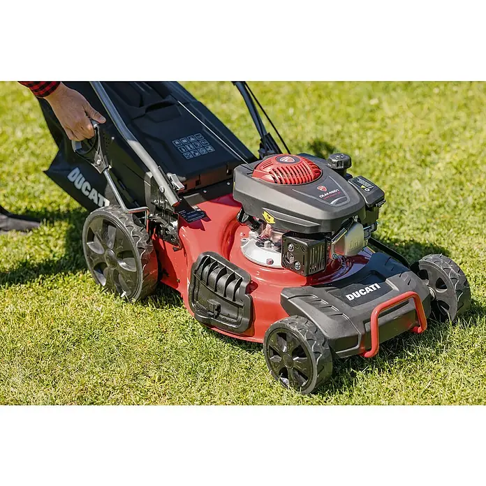 Ducati Cortacésped de gasolina DLM4601 - 2,4 kW, 150 cm³, Ancho de corte: 46 cm - El cortacésped Ducati está sobre una hierba. El aparato de jardinería es rojo y negro y lo maneja una persona.