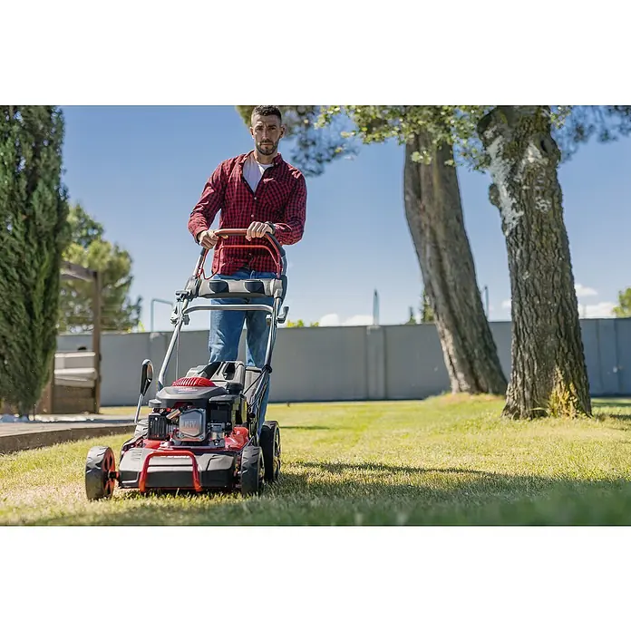 Ducati Cortacésped de gasolina DLM4601 - 2,4 kW, 150 cm³, Ancho de corte: 46 cm - Hombre cortando el césped con una cortadora de césped roja en el jardín. La cortadora de césped es el producto principal.