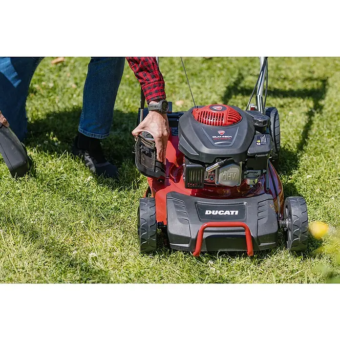 Ducati Cortacésped de gasolina DLM4601 - 2,4 kW, 150 cm³, Ancho de corte: 46 cm - Cortacésped Ducati DLM 4601 en acción: Un hombre arranca el cortacésped rojo y negro sobre un césped verde.