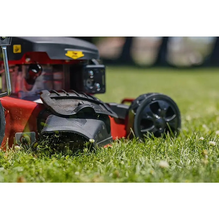 Ducati Cortacésped de gasolina DLM4601 - 2,4 kW, 150 cm³, Ancho de corte: 46 cm - Primer plano de una cortadora de césped roja en acción cortando el césped, con un enfoque en la plataforma de corte y las cuchillas afiladas.