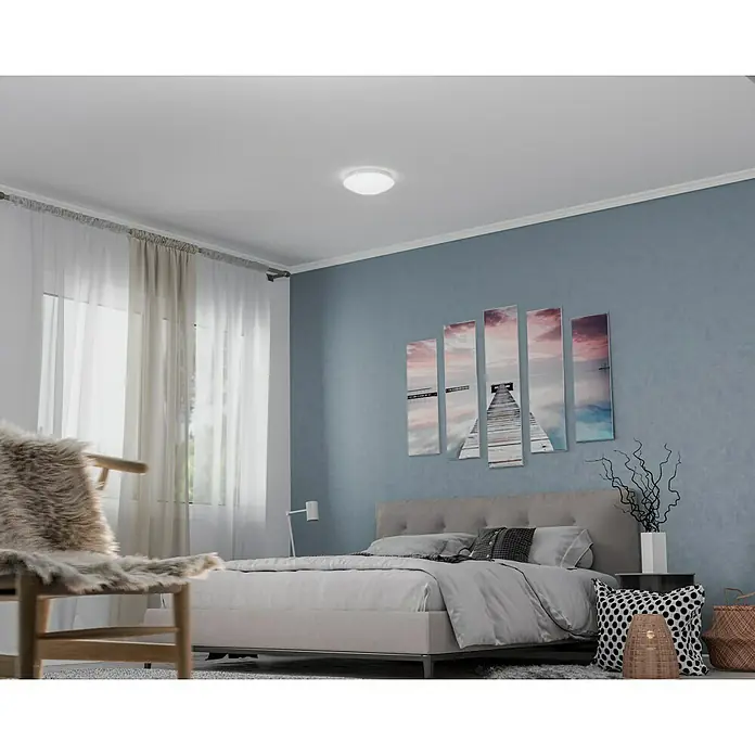 Steinel Sensor-Wand- & Deckenleuchte RS 16 L weiß - 60 W, L x B x H: 27,5 x 27,5 x 9,5 cm, Weiß, E27 - Das Bild zeigt eine moderne LED-Deckenleuchte in einem Schlafzimmer, die für helles, gleichmäßiges Licht sorgt und das Ambiente verbessert.