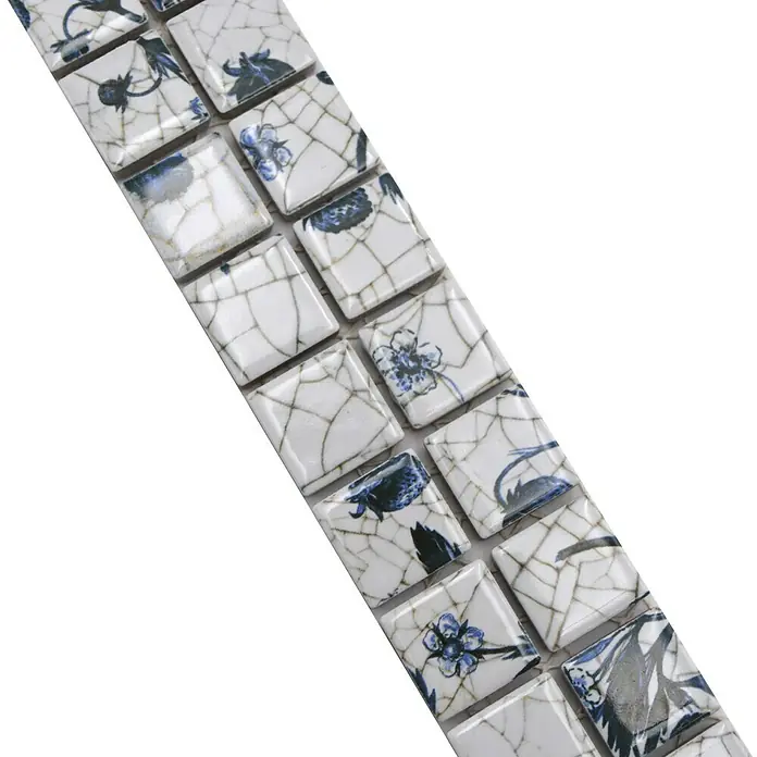 Fliesenbordüre Strawberry YBO BERRY - 29,8 x 4,8 cm, Weiß/Blau, Matt - Das Bild zeigt eine Nahaufnahme von quadratischen Mosaikfliesen mit einem Craquelé-Effekt und blauen Blumenmotiven auf weißem Grund.