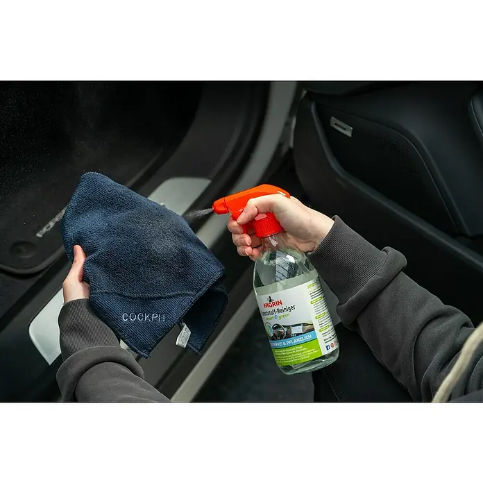 Nigrin Kunststoff-Reiniger SMART `N GREEN - 500 ml - Detailaufnahme einer Hand, die einen Nigrin Kunststoff-Reiniger auf ein Cockpit-Tuch sprüht, zur Reinigung des Auto-Innenraums.