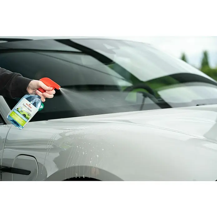 Nigrin Neutral-Reiniger SMART `N GREEN Trocken-Wäsche - 500 ml - Eine Hand sprüht Nigrin Trockenwäsche auf ein weißes Auto. Das Produkt verspricht eine schnelle und effektive Reinigung ohne Wasser.