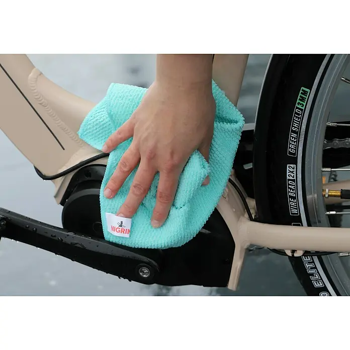 Nigrin Fahrradreiniger SMART'N GREEN - 750 ml - Ein hellblaues Nigrin Mikrofasertuch wird verwendet, um ein beigefarbenes Fahrrad zu putzen, wobei der Fokus auf dem Nigrin-Logo liegt.