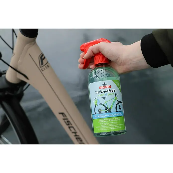 Nigrin Neutral-Reiniger SMART'N GREEN Trocken-Wäsche - 500 ml - Nahaufnahme einer Hand, die ein Fahrradreinigungsspray von Nigrin Trocken-Wäsche smart & green auf ein Fischer-Fahrrad sprüht.