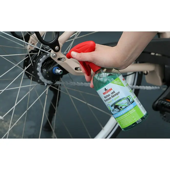 Nigrin Bremsen- & Teilereiniger SMART'N GREEN - 500 ml - Eine Hand sprüht Nigrin Ketten- und Bremsen-Reiniger auf die Kette eines Fahrrads. Das Produkt verspricht smarte, grüne Reinigung.