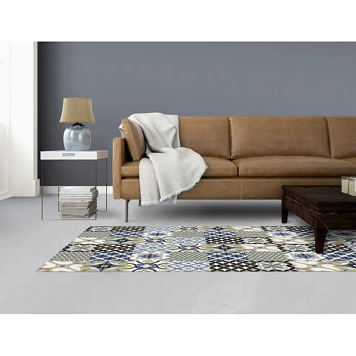 Alfombra de vinilo Croma hidraúlico - Multicolor, 150 x 80 cm - Una sala de estar elegante con un sofá de cuero marrón y una alfombra de patchwork colorida que añade un toque de vitalidad al espacio.