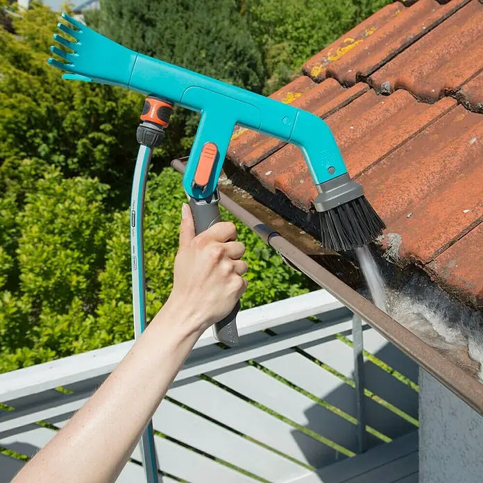 Gardena Combisystem Dachrinnenreiniger - Passend für: Gardena Combisystem Stiele - Eine Person benutzt eine GARDENA Dachrinnenbürste zur Reinigung, umgeben von üppigem Grün und Ziegeldächern.