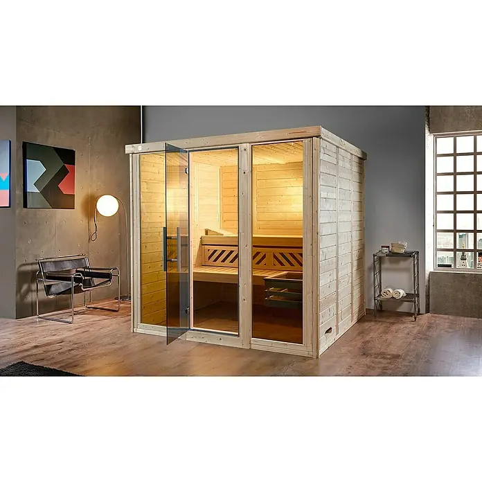 Weka Massivholzsauna Kemi Panorama - Mit 7,5 kW Bio-Aktiv-Ofen mit externer digitaler Steuerung, L x B x H: 210 x 211 x 200 cm, Natur - Innenaufnahme einer Sauna mit Holzbänken und Glasfront, die einladend und entspannend wirkt. Die Sauna wird durch ein warmes Licht beleuchtet.