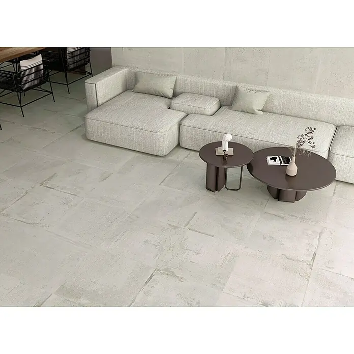 Feinsteinzeugfliese Bond White - 60 x 60 cm, Weiß, Matt - Ein modernes Wohnzimmer mit einem hellen modularen Sofa und zwei runden Couchtischen auf einem hellen, strukturierten Fliesenboden.