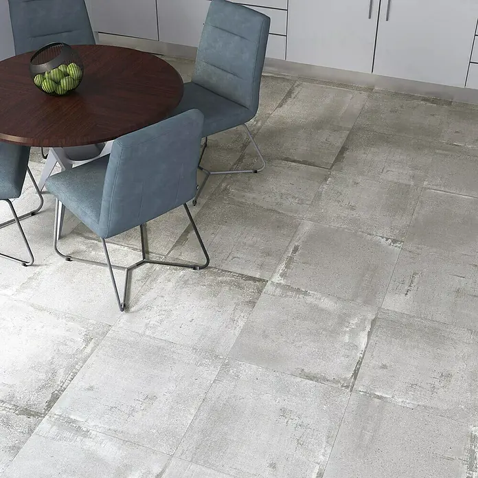 Feinsteinzeugfliese Bond Ash - 60 x 60 cm, Grau, Matt - Nahaufnahme eines Essbereichs mit grauem Fliesenboden, einem Holztisch und blauen Stühlen. Elegantes Design für moderne Innenräume.