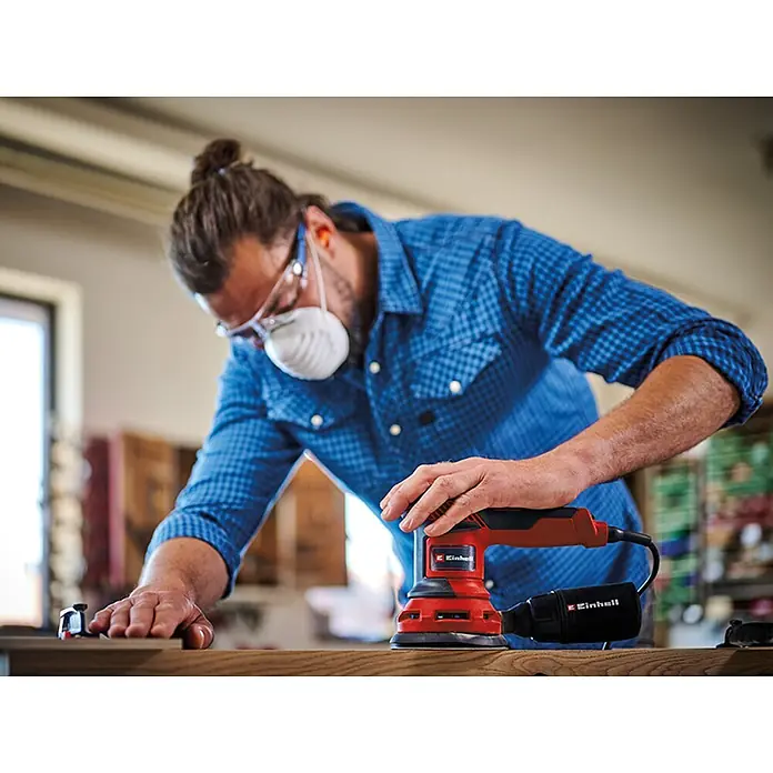 Einhell Classic Lijadora excéntrica eléctrica TC-RS 425 E - 425 W, Diámetro disco de lija: 125 mm - Un hombre lijando madera con una lijadora orbital aleatoria roja Einhell, que está colocada sobre la pieza de trabajo. Lleva equipo de protección.