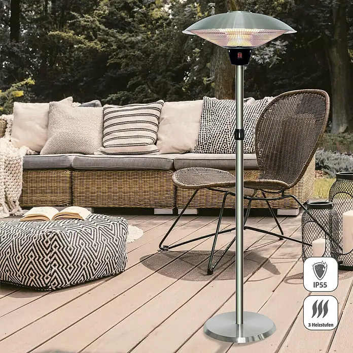 Voltomat HEATING Halogen-Heizstrahler - 46 x 46 x 205 cm, 2.100 W, Silber - Ein schlanker, silberner Terrassenheizer sorgt für Wärme und Ambiente auf der Terrasse. Er steht auf einem Holzdeck mit Loungemöbeln.