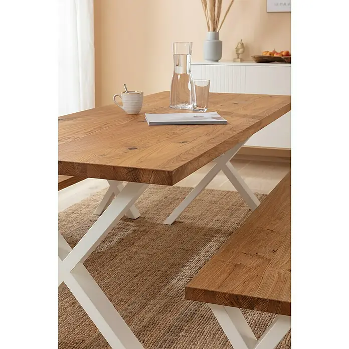 Pur Iternal Select Tischplatte Vintage - 200 x 80 x 4 cm, Eiche - Nahaufnahme eines Esstisches aus Holz mit weißen Beinen, darauf eine Karaffe Wasser, ein Glas, eine Tasse und ein Buch.