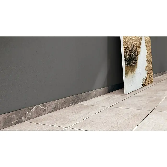 Sockelfliese Premium Marble - 7 x 80 cm, Grau, Glänzend - Detailansicht des Bodenbelags und der Sockelleisten in einem Raum, mit einem Kunstwerk, das gegen die Wand gelehnt ist.