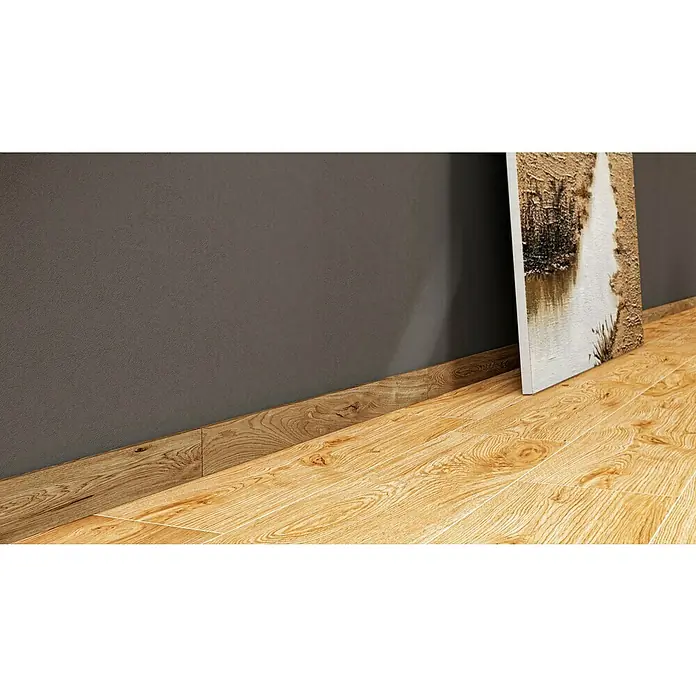 Atlas Concorde Solution Sockelfliese Whirl Natural - 7,2 x 90 cm, Braun, Matt - Detailaufnahme von Holzfußleiste, die den Übergang zwischen brauner Wand und hellem Holzboden akzentuiert, ergänzt durch ein abstraktes Gemälde.