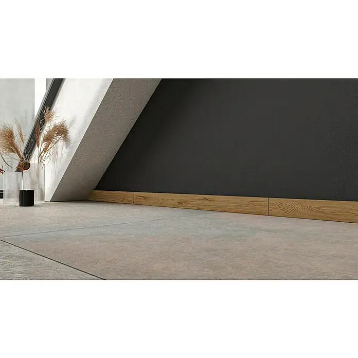 Atlas Concorde Solution Sockelfliese Twist Rovere - 7,2 x 90 cm, Beige, Matt - Innenaufnahme mit einem Holzsockel, der an einer grauen Wand mit Bodenfliesen befestigt ist, neben einer Pflanze in einer Vase.