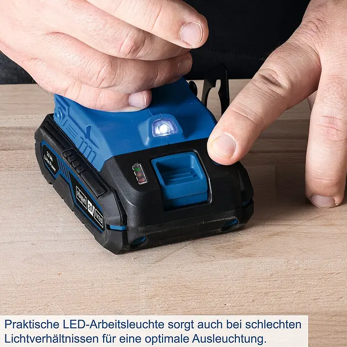 Scheppach IXES 20V Akku-Bohrschrauber-Set C-DTB74/1-X - 20 V, 1 Akku, 2 Ah, 50 Nm, 74-tlg. Zubehör-Set - Nahaufnahme einer scheppach 20 V / 2,0 Ah Akku mit LED-Arbeitsleuchte, die von einer Hand bedient wird, auf einem Holztisch.