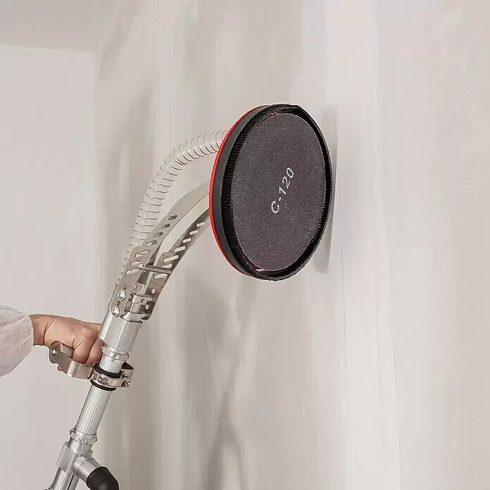 Wolfcraft Disco de lijado - Diámetro: 225 mm, Grano: 220 mm - Mano sosteniendo una lijadora de poste plateada con cabezal circular rojo y negro y manguera transparente, lijando una pared.
