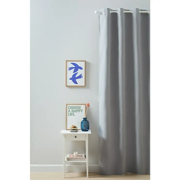 Cortina con ollaos Blackout - An x Al: 140 x 260 cm, Gris - Una cortina gris cuelga junto a una mesita de noche blanca con decoración y dos cuadros en la pared, complementando el ambiente de la habitación.