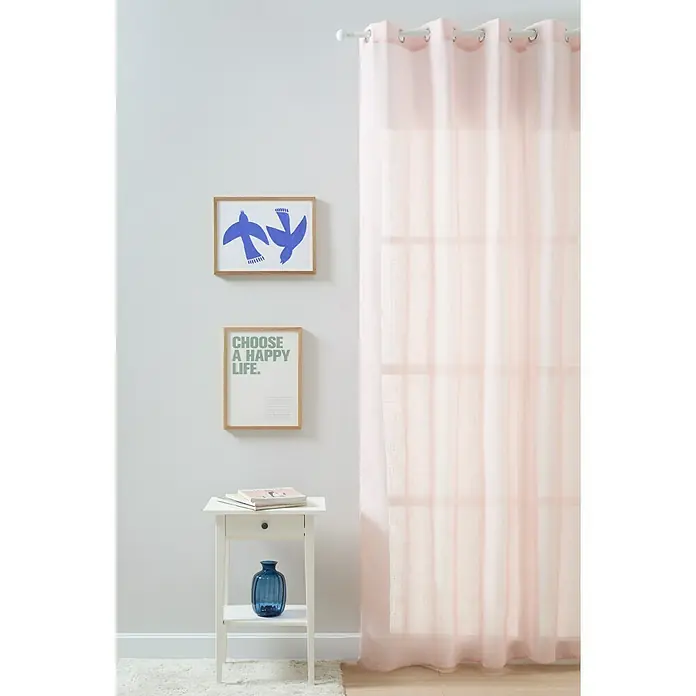Visillo para ventana Kyos - 200 x 270 cm, 100% poliéster, Rosa - Una cortina traslúcida de color rosa claro cuelga frente a una ventana, dejando entrar luz suave. Un arte mural decorativo y una mesa auxiliar completan el ambiente.