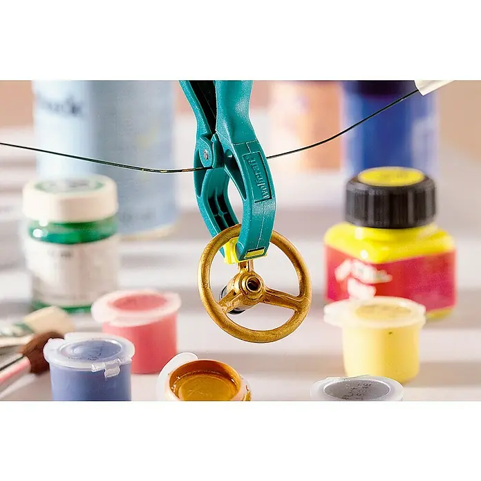 Wolfcraft Federzwinge Microfix - Spannweite: 30 mm, Ausladung: 30 mm - Eine goldene Steuerrad-Miniatur wird mit einer grünen Klemme gehalten, umgeben von Farbtiegeln. Ideal für Modellbau-Enthusiasten und detailverliebte Bastler.