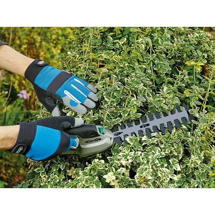 Gardol Gartenhandschuhe Geräte - 8, Blau - Nahaufnahme einer Person, die mit einer Gardol-Heckenschere eine Hecke schneidet und dabei blaue und graue Gartenhandschuhe trägt.