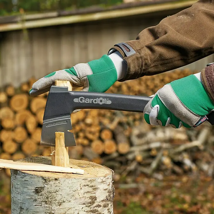 Gardol Gartenhandschuhe Geräte - 10, Grün - Nahaufnahme einer Person mit einer Gardol-Axt, die Holz spaltet, wobei der Fokus auf der Axt und dem Holz liegt.