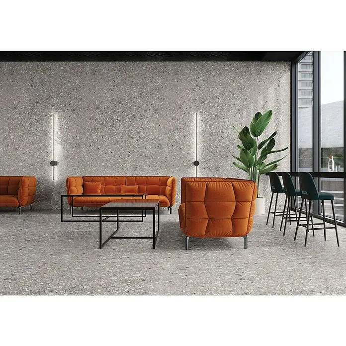 Feinsteinzeugfliese Terrazzo Ceppo - 119,7 x 119,7 cm, Silber, Glänzend - Moderne Lobby mit Terrazzoboden und Wand, orangen Sofas und Barhockern. Das minimalistische Design strahlt Eleganz und Komfort aus.